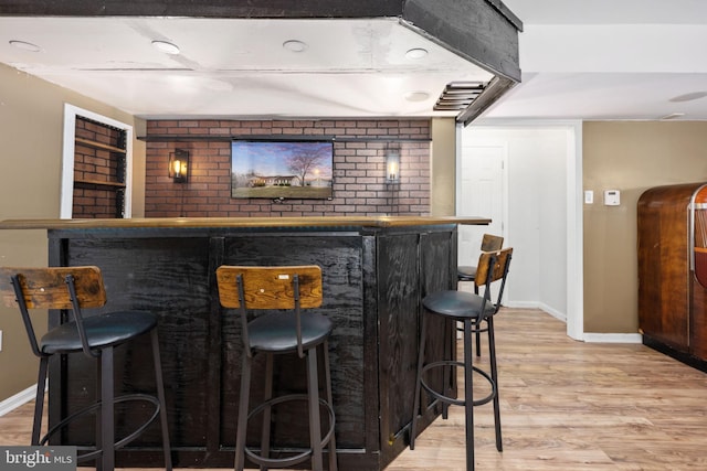 bar with a dry bar, baseboards, and light wood finished floors