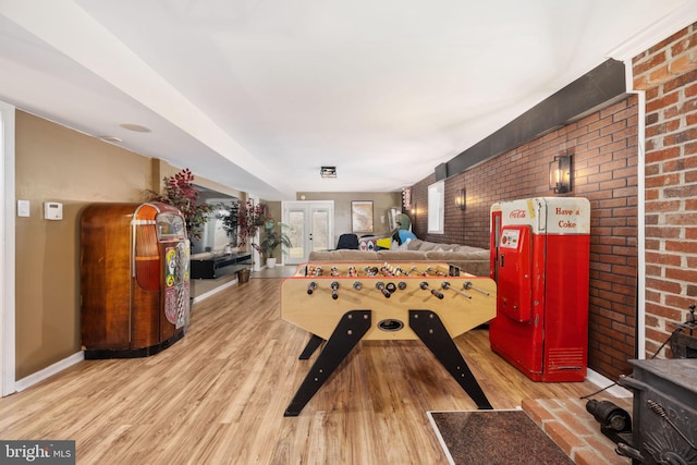 playroom with brick wall, baseboards, french doors, a wood stove, and wood finished floors