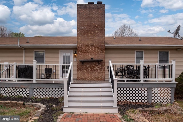 back of property with a deck, roof with shingles, and a chimney