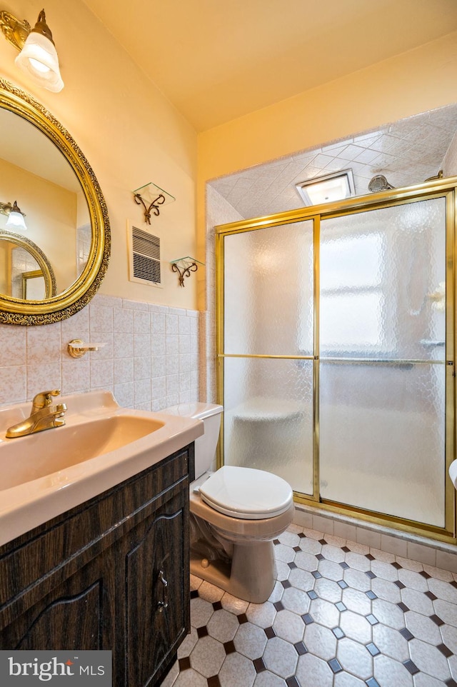 bathroom featuring vanity, a wainscoted wall, a stall shower, tile walls, and toilet