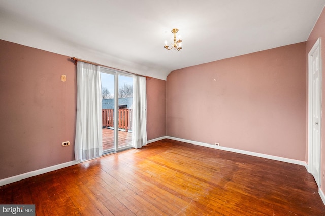 spare room with lofted ceiling, baseboards, wood-type flooring, and a chandelier