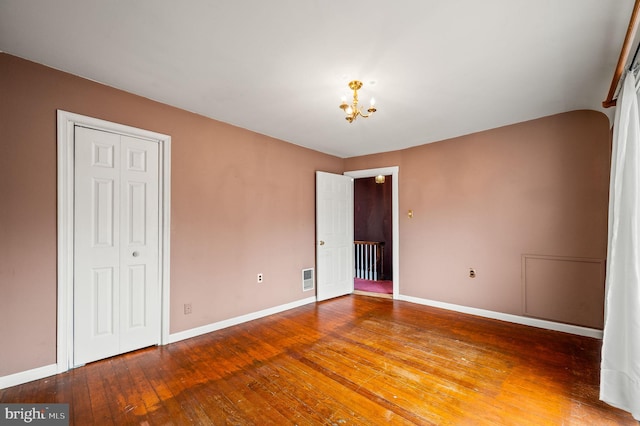 unfurnished bedroom with a closet, baseboards, a notable chandelier, and hardwood / wood-style flooring