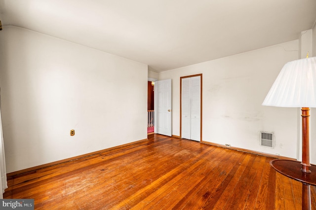 empty room featuring visible vents, wood-type flooring, and vaulted ceiling