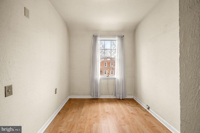 spare room featuring light wood-style flooring, a textured wall, and baseboards