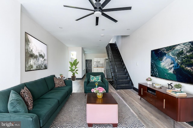 living area featuring stairs, a ceiling fan, and light wood finished floors