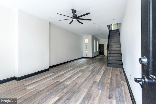 unfurnished living room with baseboards, wood finished floors, ceiling fan, and stairs