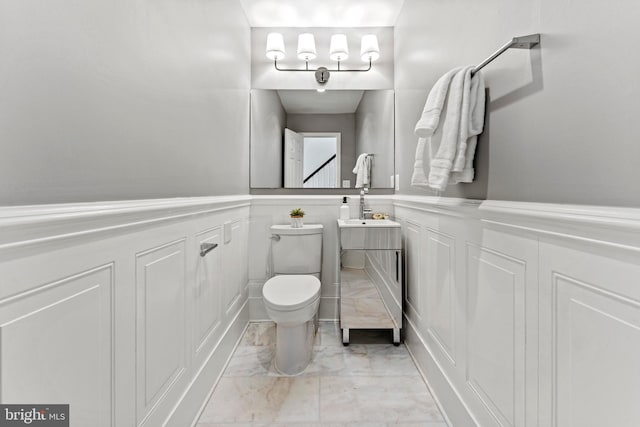 bathroom featuring a wainscoted wall, toilet, marble finish floor, a decorative wall, and vanity