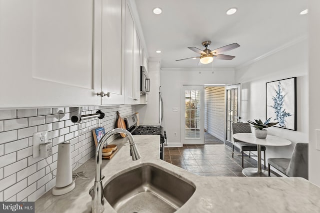 kitchen featuring crown molding, light stone counters, appliances with stainless steel finishes, white cabinets, and a sink