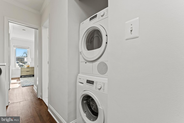 washroom with stacked washer and clothes dryer, ornamental molding, dark wood finished floors, baseboards, and laundry area