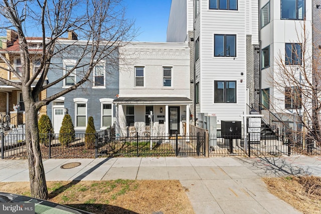 multi unit property featuring a porch, brick siding, and a fenced front yard