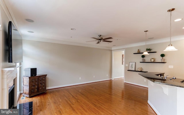 living area featuring baseboards, wood finished floors, ceiling fan, and ornamental molding