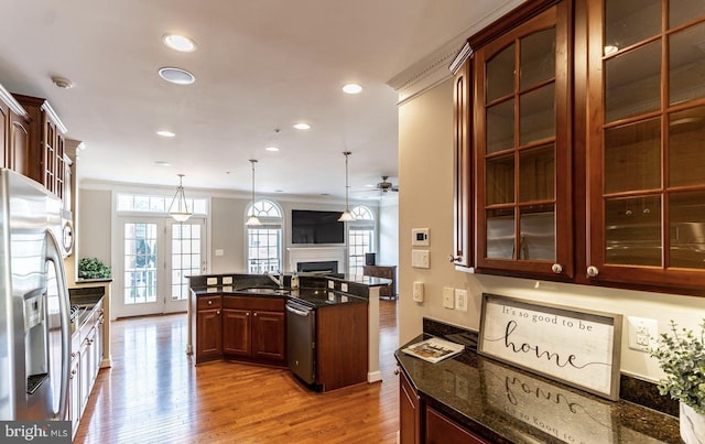 kitchen featuring light wood-style flooring, dark stone countertops, appliances with stainless steel finishes, a fireplace, and glass insert cabinets