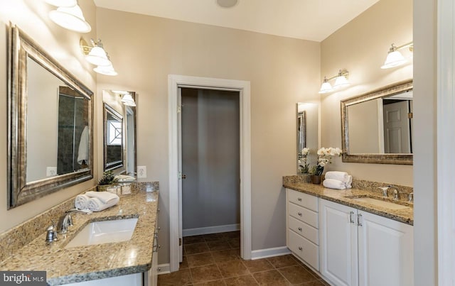 full bath featuring tile patterned flooring, two vanities, baseboards, and a sink