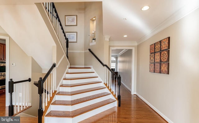 stairs with recessed lighting, wood finished floors, baseboards, and ornamental molding