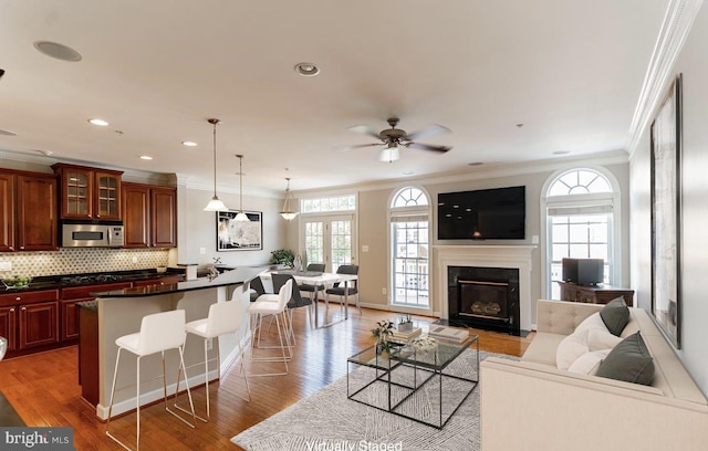 living room with a ceiling fan, recessed lighting, light wood-style floors, a glass covered fireplace, and crown molding