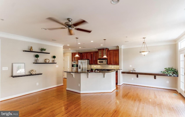 kitchen with a ceiling fan, a breakfast bar, appliances with stainless steel finishes, crown molding, and tasteful backsplash