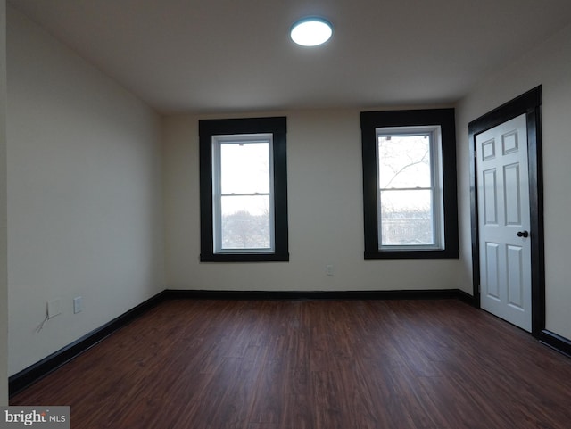 spare room with baseboards and dark wood-type flooring