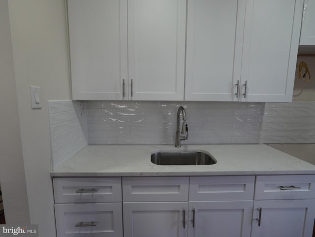 kitchen with light stone counters, decorative backsplash, white cabinets, and a sink