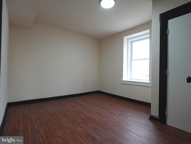 unfurnished room with dark wood-type flooring and baseboards