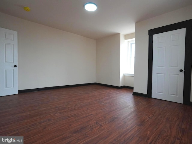 spare room featuring dark wood-style floors and baseboards