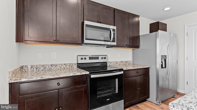 kitchen with stainless steel appliances, light stone countertops, dark brown cabinetry, and light wood-style flooring