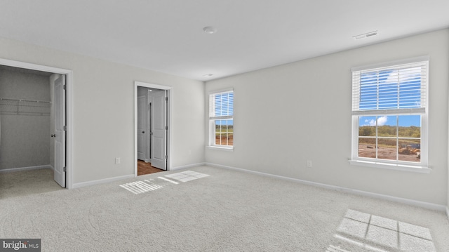 unfurnished bedroom featuring visible vents, a walk in closet, baseboards, carpet floors, and a closet