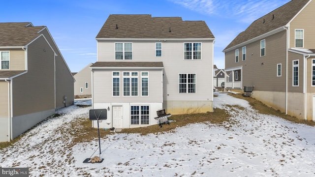 snow covered rear of property with central air condition unit and a shingled roof