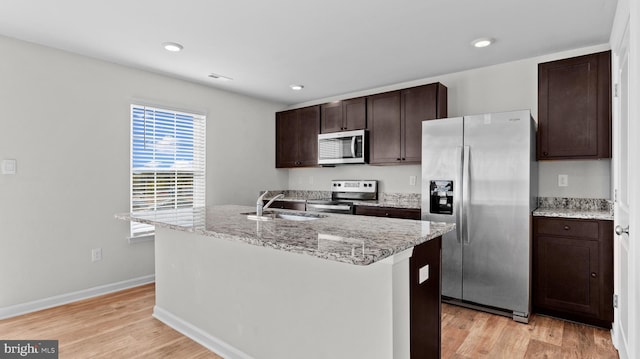 kitchen with dark brown cabinets, an island with sink, light wood-type flooring, appliances with stainless steel finishes, and a sink