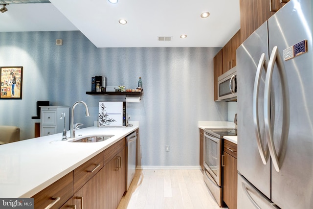 kitchen featuring brown cabinetry, wallpapered walls, stainless steel appliances, and a sink