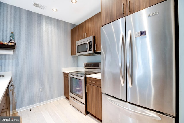 kitchen featuring stainless steel appliances, brown cabinets, visible vents, and wallpapered walls