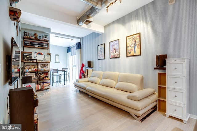 living area featuring wallpapered walls, beam ceiling, rail lighting, and light wood finished floors