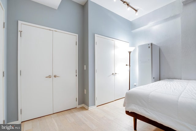 bedroom featuring light wood-style flooring, rail lighting, and two closets