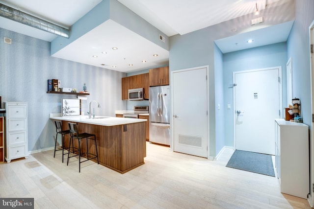 kitchen with a breakfast bar, stainless steel appliances, a peninsula, brown cabinetry, and light countertops