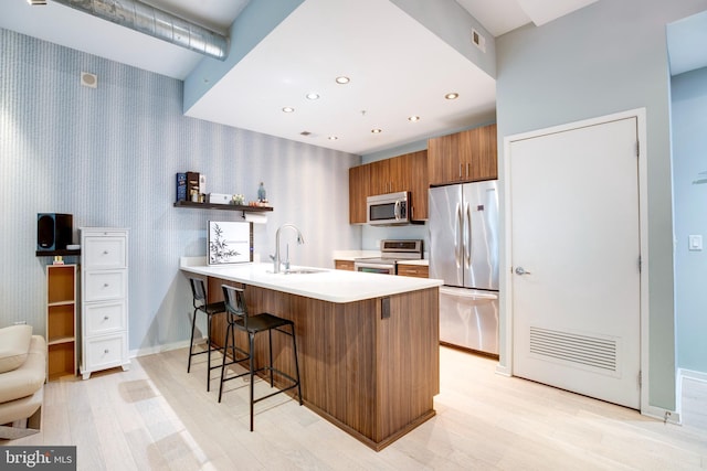 kitchen featuring brown cabinets, a breakfast bar, a peninsula, appliances with stainless steel finishes, and wallpapered walls