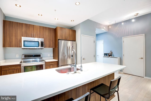 kitchen featuring a sink, appliances with stainless steel finishes, brown cabinetry, light wood finished floors, and light countertops