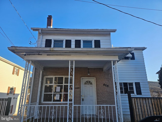 view of front of property featuring brick siding, covered porch, a chimney, and fence