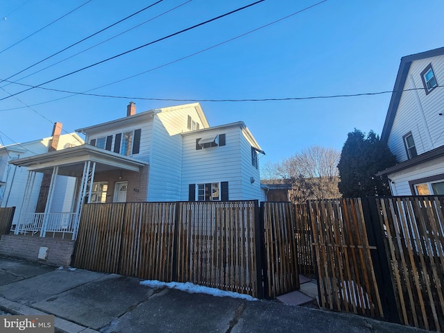 view of side of home with a fenced front yard, covered porch, and a chimney