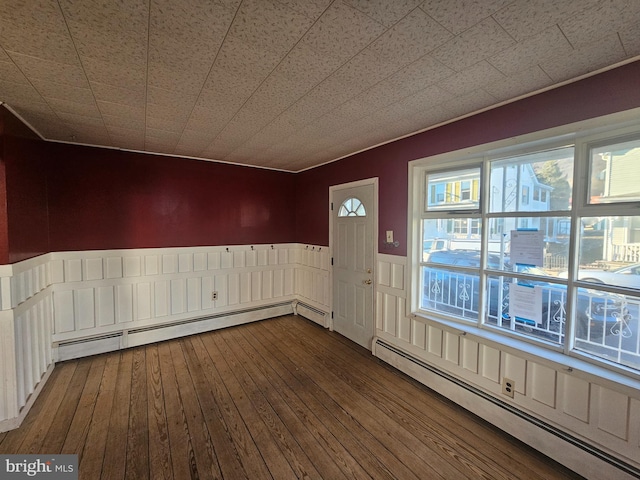 unfurnished dining area featuring a baseboard heating unit, dark wood finished floors, and wainscoting