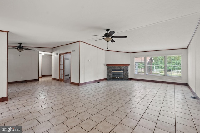 unfurnished living room featuring a stone fireplace, crown molding, light tile patterned floors, and a ceiling fan