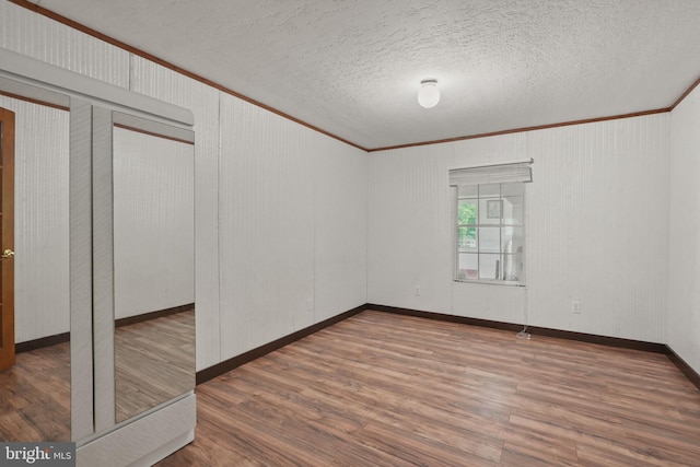 spare room featuring a textured ceiling, wood finished floors, baseboards, and ornamental molding