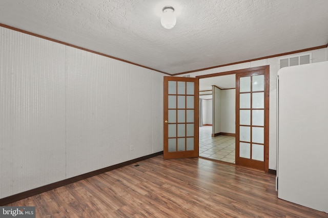 empty room featuring wood finished floors, visible vents, french doors, a textured ceiling, and crown molding