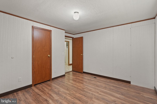 unfurnished bedroom with visible vents, a textured ceiling, wood finished floors, crown molding, and baseboards