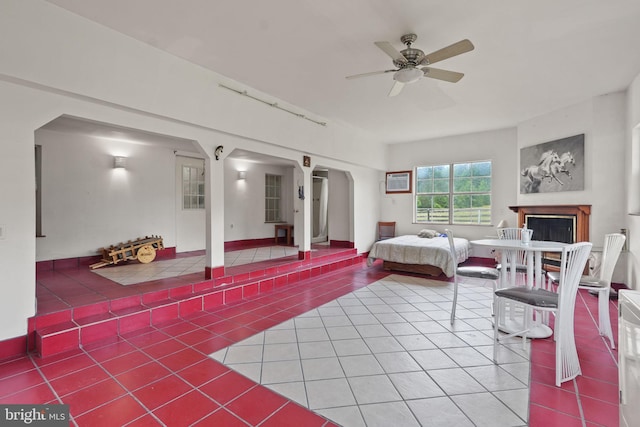 tiled bedroom featuring arched walkways, a fireplace, an AC wall unit, and ceiling fan