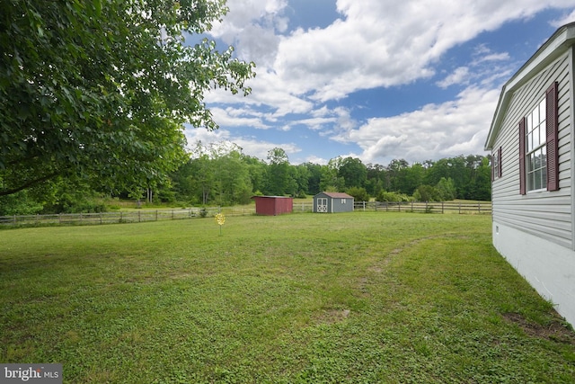 view of yard with an outbuilding, a storage shed, fence, and a rural view