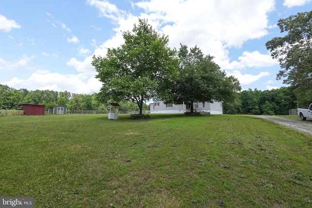 view of yard featuring a storage unit, an outbuilding, driveway, and fence