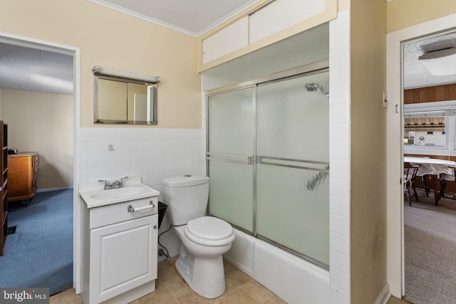 ensuite bathroom with crown molding, toilet, vanity, wainscoting, and tile walls