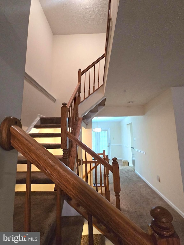 stairway featuring carpet flooring, a textured ceiling, and baseboards