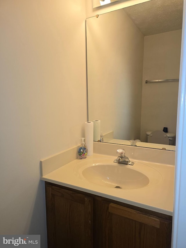 half bathroom featuring vanity, toilet, and a textured ceiling