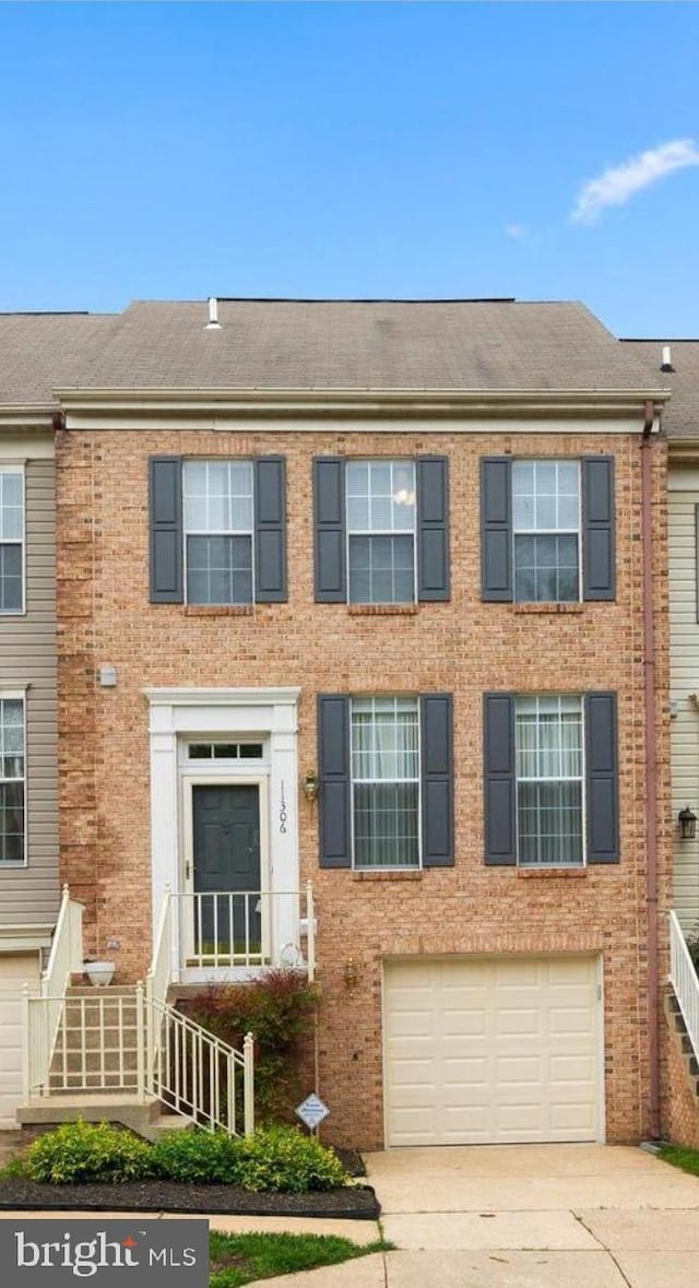 view of property with an attached garage, brick siding, driveway, and a shingled roof