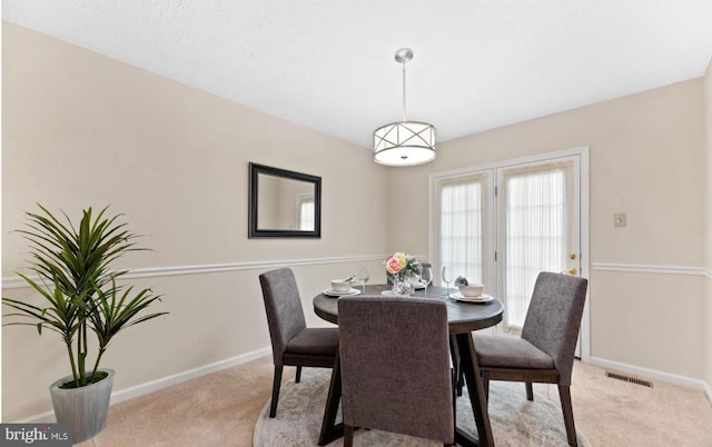 dining room with light carpet, visible vents, and baseboards